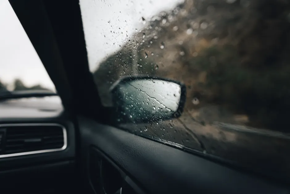 Pluies orageuses en Algérie : 16 wilayas concernées de 15 h à minuit View from car interior with raindrops on window, focusing on the side mirror and road outside.