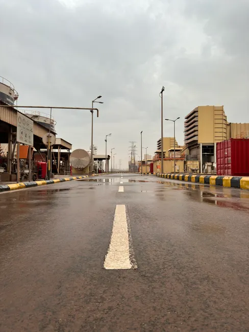 Wet road in an industrial area after rain, showcasing power plant structures under a cloudy sky.